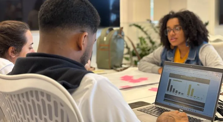 Jovens reunidos em uma mesa analisando gráficos em um notebook