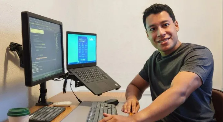 Jovem sorrindo em uma estação de trabalho com computadores