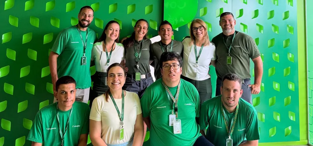 Equipe reunida em frente a uma parede verde com recortes de folhas
