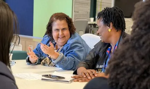 Mulheres conversando e gesticulando ao redor de uma mesa de reunião