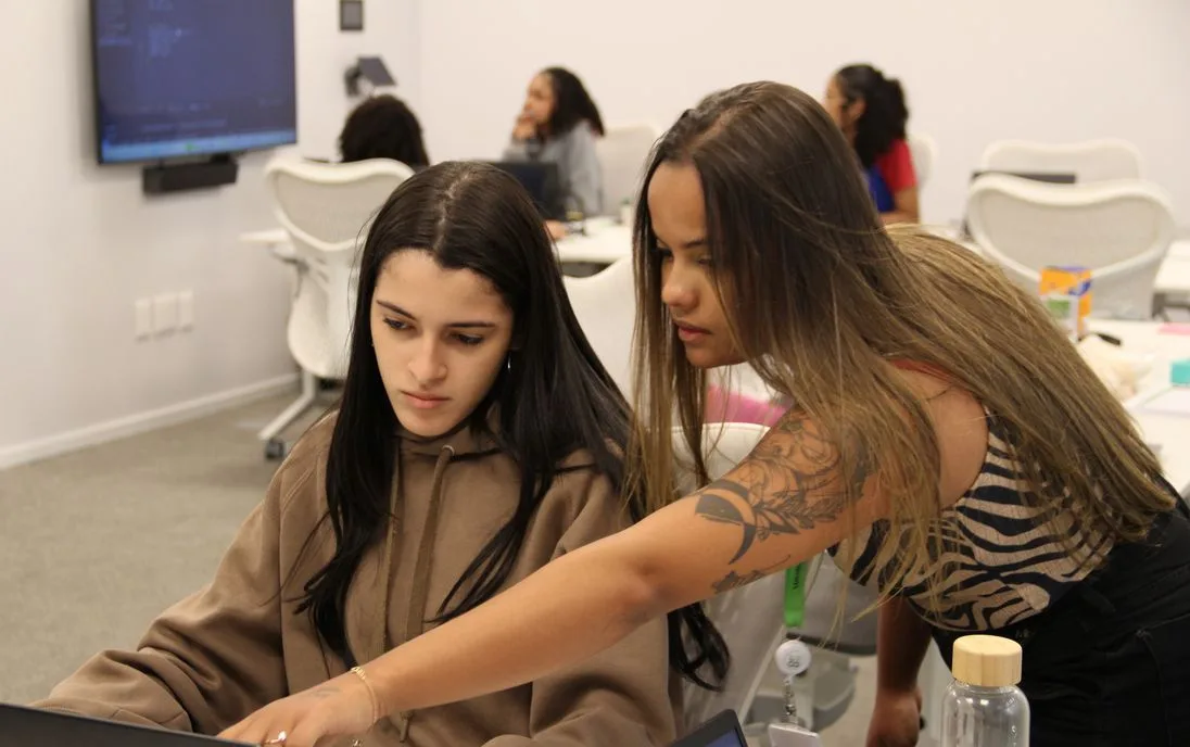 Voluntária orientando uma jovem em frente ao notebook